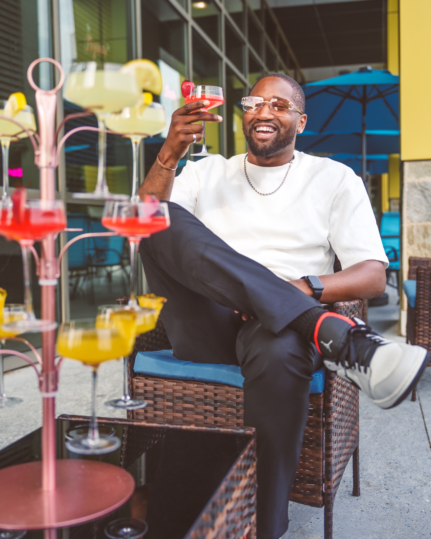 Guest raising a cocktail beside a colorful drink tower on the patio